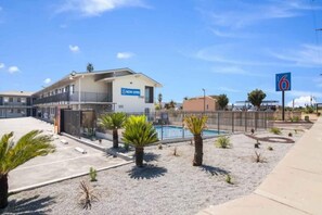Un motel doté d’une piscine, d’un parking clôturé et surplombé d’un ciel bleu azur.