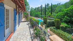 Ein balkon mit Steinplatten, einer Holz-Pergola, einem Pool und einem gepflegten Garten mit Hecken und Bäumen.