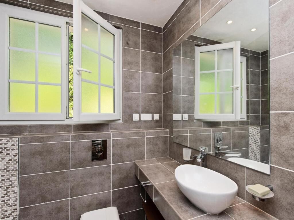 Un baño moderno con un espejo grande, un lavamanos blanco y una ventana con vidrio esmerilado.