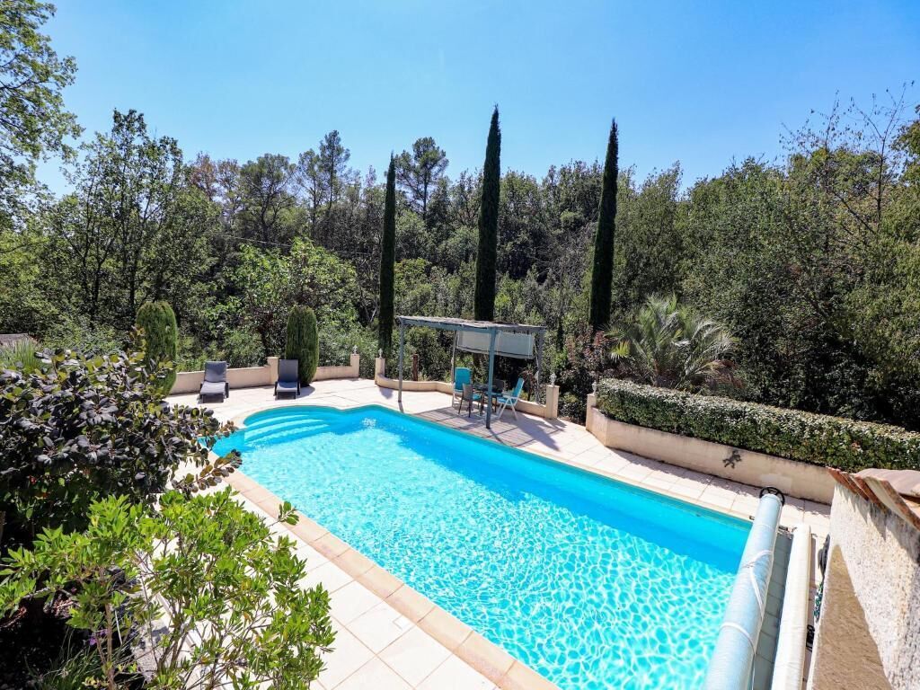 A swimming pool with lounge chairs and a covered seating area, surrounded by greenery and trees.
