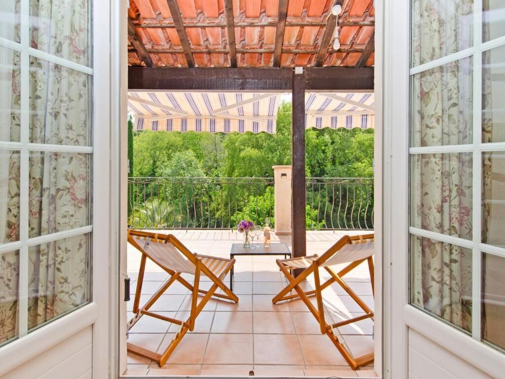 Un balcon avec deux chaises en bois, une petite table sur laquelle est posé un vase, et une vue sur la verdure et les bâtiments.