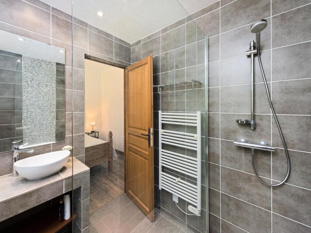 Een moderne badkamer met een douchecabine van glas, een witte handdoekhouder en een houten deur.
