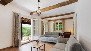 Ein Wohnzimmer mit einer Couch, einem Couchtisch und einer Chandelüstere. Eine Glastür ermöglicht den Zugang zu einem Außenbereich.