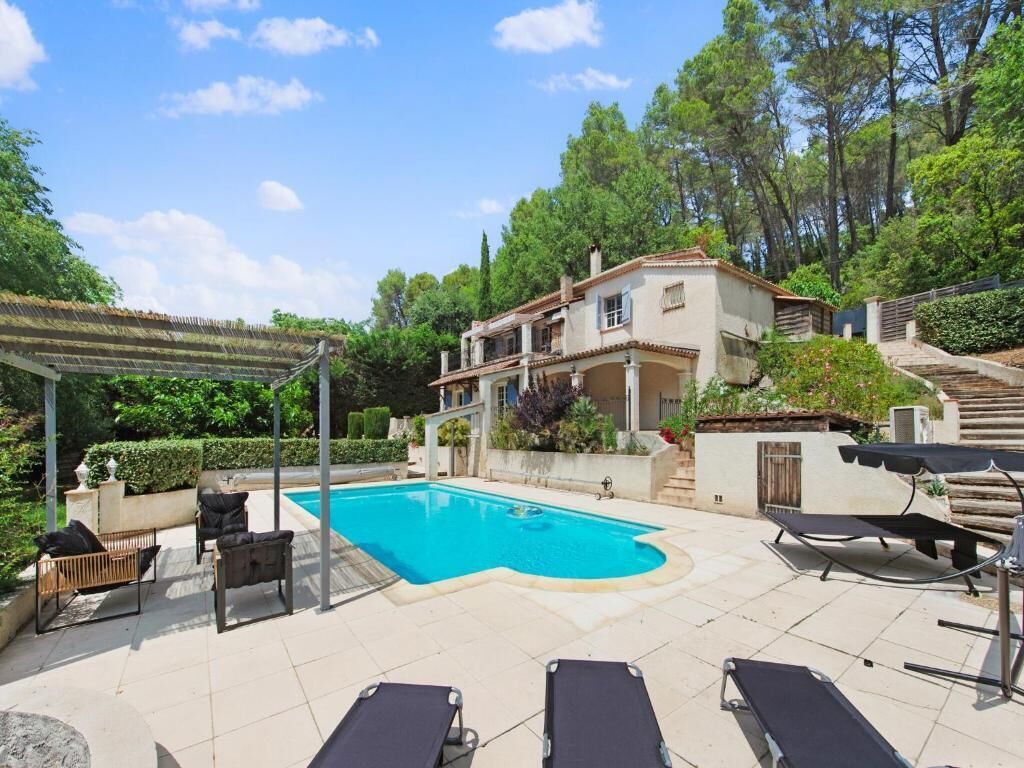 Zona de piscina con sillones de descanso, una pérgola y una casa con techo de tejas.