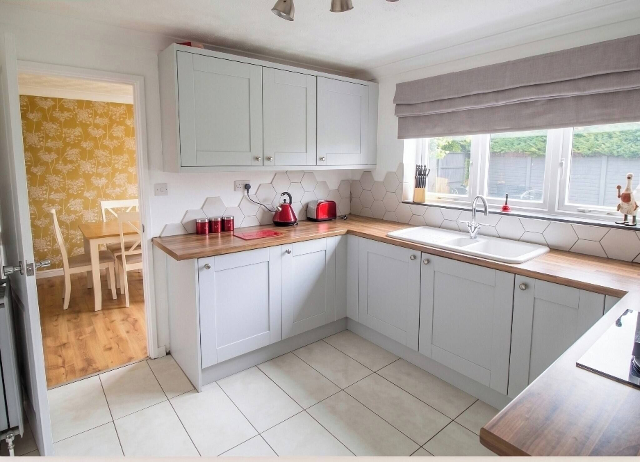 A kitchen with white cabinets, a wooden countertop, a red kettle, and a window with a view.