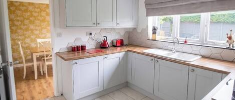A kitchen with white cabinets, a wooden countertop, a red kettle, and a window with a view.