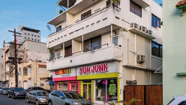 Un edificio de varios pisos con una fachada que muestra el nombre 'YUM JUNK' y un cartel que anuncia 'Poke Bowls'.