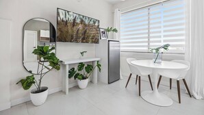 Una cocina moderna con televisor de pantalla plana, armarios blancos, refrigerador de acero inoxidable y comedor con mesa y sillas blancas.