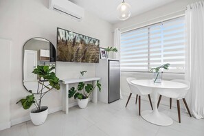 Eine moderne Küche mit Flachbildfernseher, weißen Schränken, einem Edelstahlkühlschrank und einem Essbereich mit weißem Tisch und Stühlen.