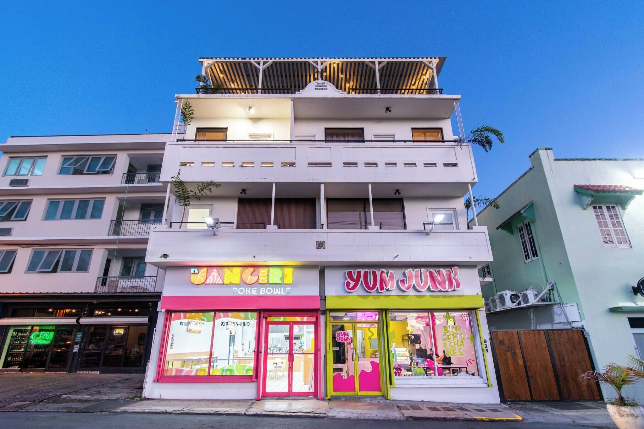 Um edifício de vários andares com um restaurante no andar térreo chamado 'Yum Junk' e um estabelecimento no segundo andar chamado 'Poke Bowls'.