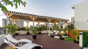Una terraza en la azotea con una pérgola, sillones de descanso, plantas en macetas y vistas de la ciudad.
