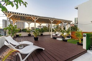 Eine Dachterrasse mit einer Pergola, Liegestühlen, Topfpflanzen und Blick auf die Stadtlandschaft.