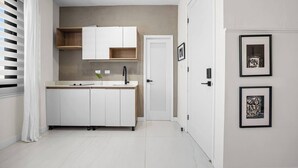 Una cocina compacta con armarios blancos, un lavamanos y una puerta que da a otra habitación. Hay obras de arte enmarcadas en la pared.