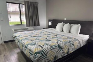 Ett hotellrum med en säng, ett fönster med gardiner, en väggmonterad luftkonditioneringsanläggning och ett nattduksbord.