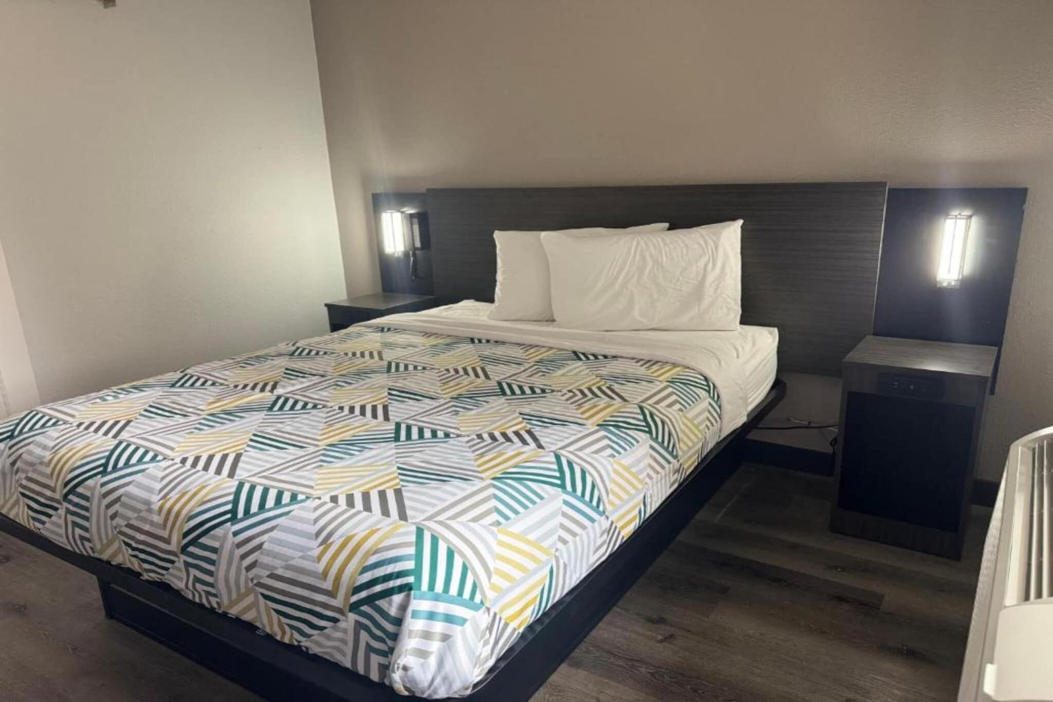 A hotel room with a bed, nightstands, and a wall-mounted light fixture.