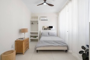 A bedroom with a bed, a ceiling fan, a bedside table with a lamp, a wooden dresser, and a plant. - Naya Sanctuary - Zenn (San Juan city)
