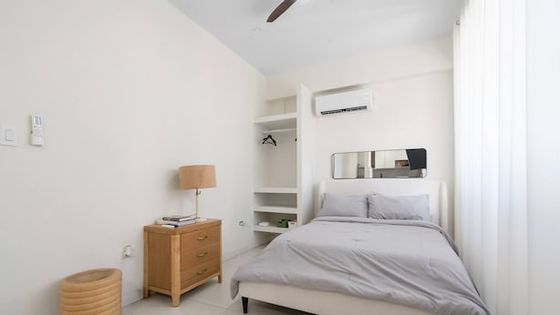 Um quarto com cama, mesa de cabeceira, luminária, guarda-roupa e estantes embutidas.