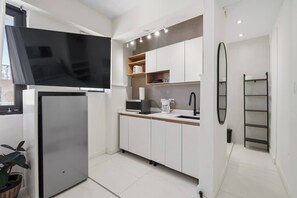 Eine moderne Küche mit Flachbildfernseher, integriertem Mikrowellenherd, Kaffeemaschine und weißen Schränken.