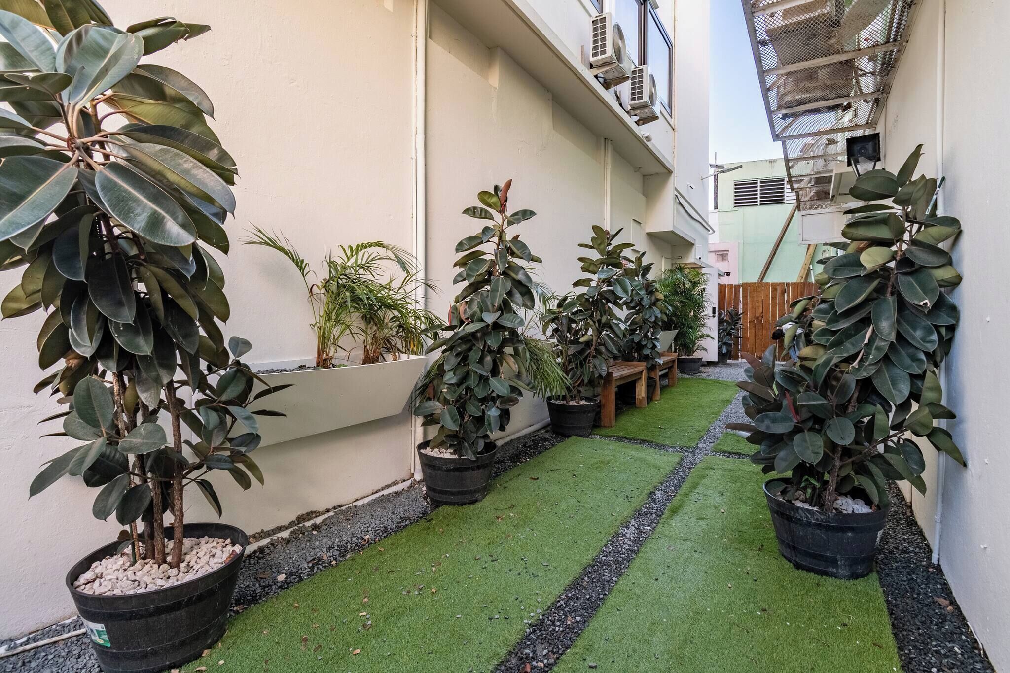 A narrow courtyard with potted plants and a green artificial turf path.