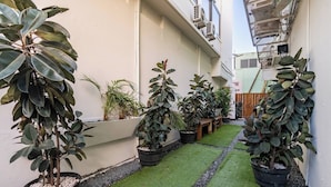 Um pátio estreito com plantas em vasos e um caminho de grama sintética verde.