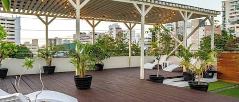 A rooftop terrace with a pergola, potted plants, and lounge chairs.