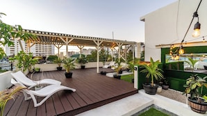 Terraço no telhado com pérgola, espreguiçadeiras, plantas em vasos e área de piscina.