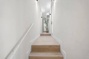Ein schmaler, hell gefliester Flur mit einer Holztreppe, die zu einer Tür mit einem Blumentopf führt.