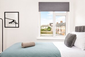 A bedroom with a bed, a window with a view of houses, a framed picture, and a rolled towel. - Blyth 4BR House | Sleeps 8 | WiFi | Crew Stay (Blyth)