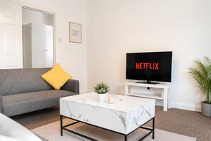 A living room with a sofa, a coffee table, a TV displaying 'NETFLIX,' a small plant, and a framed quote on the wall. - Blyth 4BR House | Sleeps 8 | WiFi | Crew Stay (Blyth)