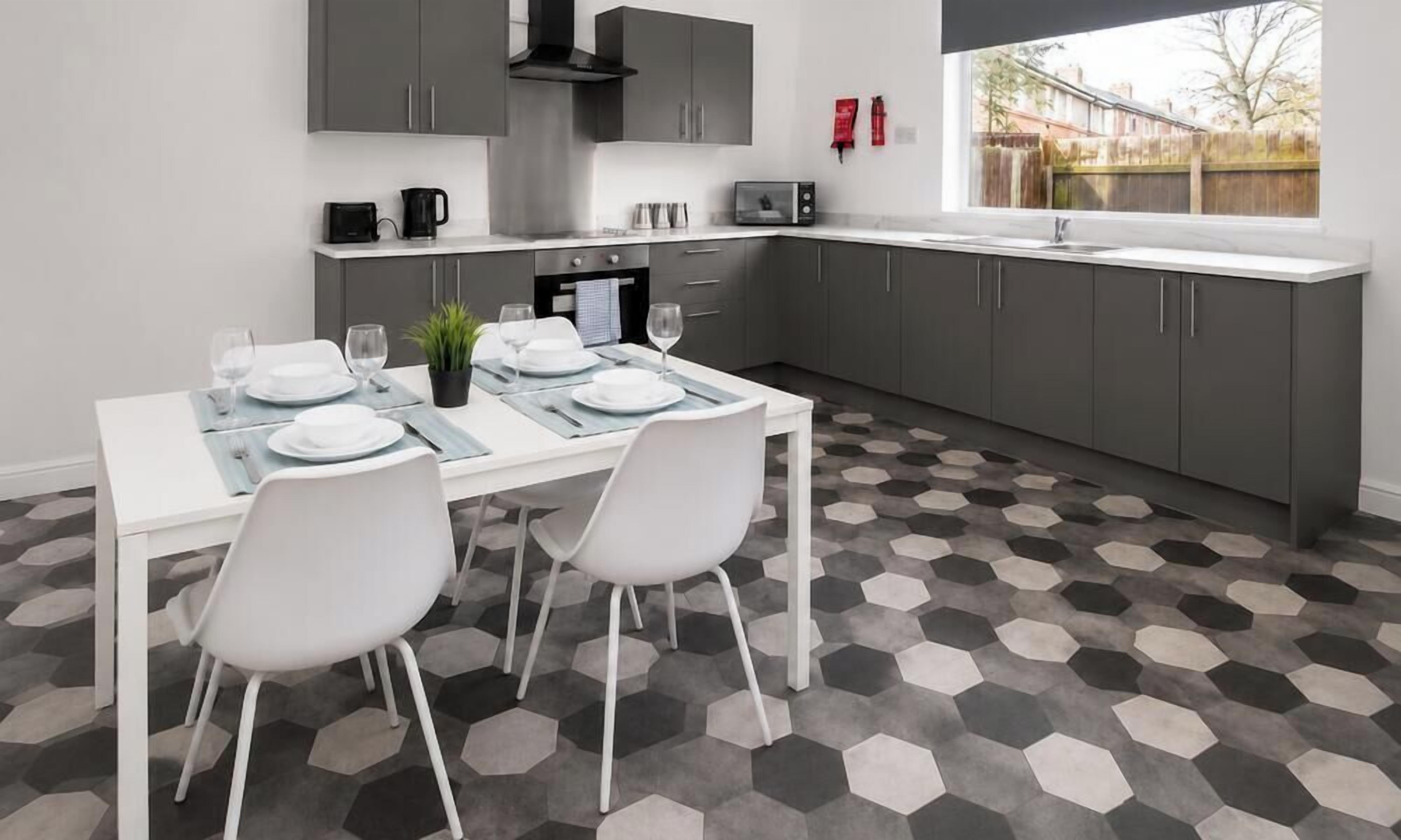 A modern kitchen with a dining table set for four, grey cabinets, and a hexagonal patterned floor.