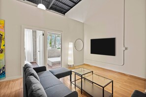 A modern living room with a sofa, a glass coffee table, a flat-screen TV mounted on the wall, and a door leading to an outdoor area. - Barrio Sanctuary - Bosque Azul (San Juan city)