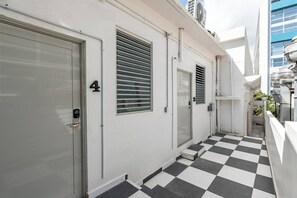 Ein schmaler Korridor mit Schachbrettfußboden, einer Tür mit der Nummer 4 und einem Fenster mit horizontalen Rollläden.