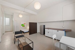A modern, well-lit room with a bed, a small table, a chair, a cabinet, and a refrigerator. - Barrio Sanctuary - Villa Serena (San Juan city)