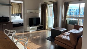Moderni hotellihuone, jossa on sänky, televisio, oleskelualue ja näkymä kaupunkiin.