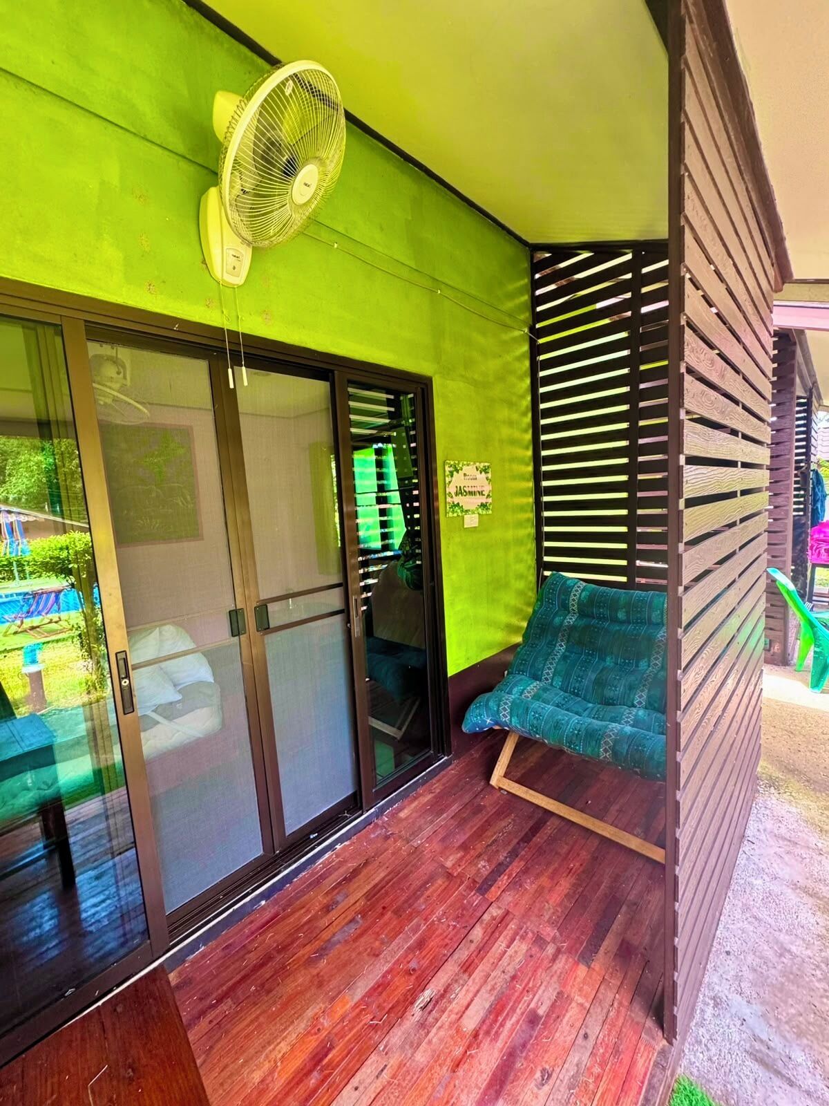 Una habitación con puerta corrediza de vidrio, un ventilador, una pared verde y un separador de madera con listones.