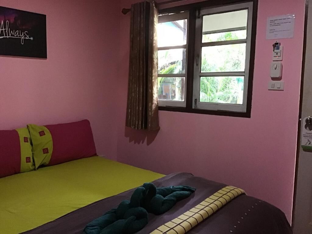 Una habitación con cama, una ventana con cortinas, un letrero en la pared y una puerta con interruptor de luz.