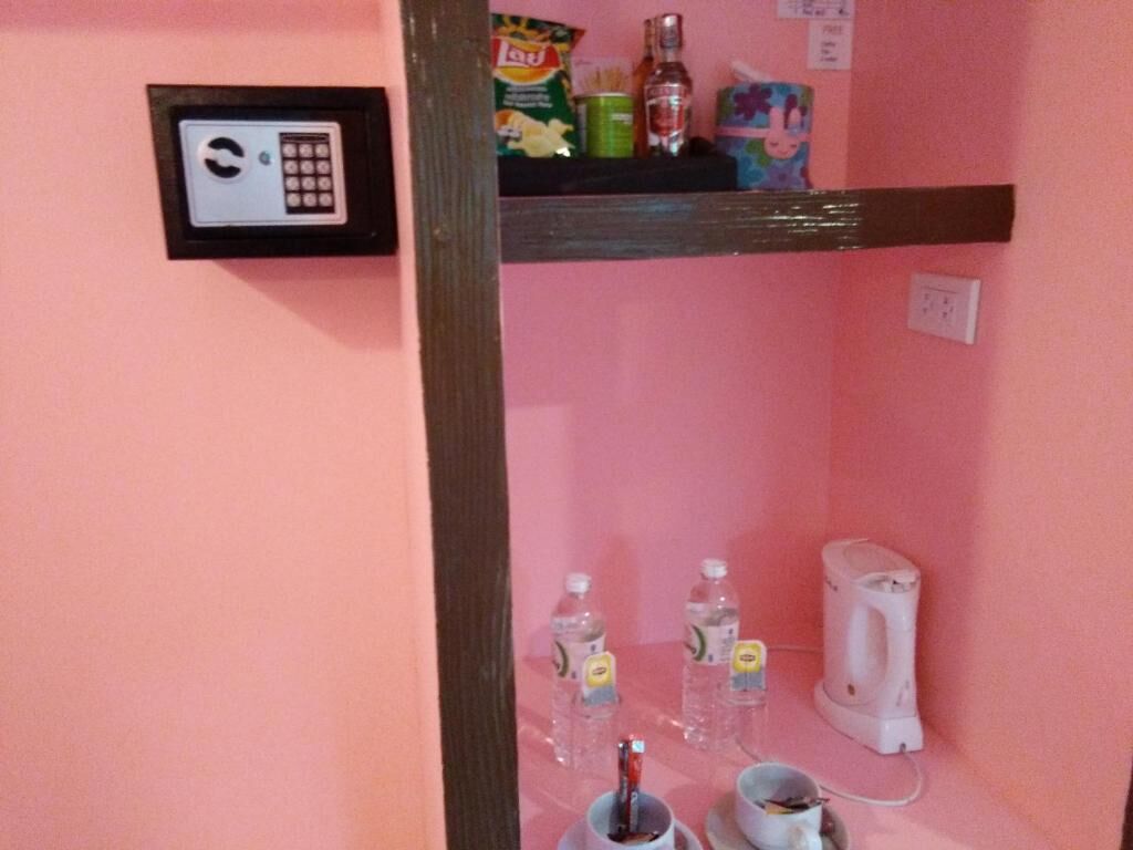 A pink wall with a security keypad, a shelf with snacks, a kettle, and two bottles of water.