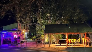 A nighttime view of a restaurant with outdoor seating, a neon sign, and a covered area. - Grand Tree Resort (Ko Chang)