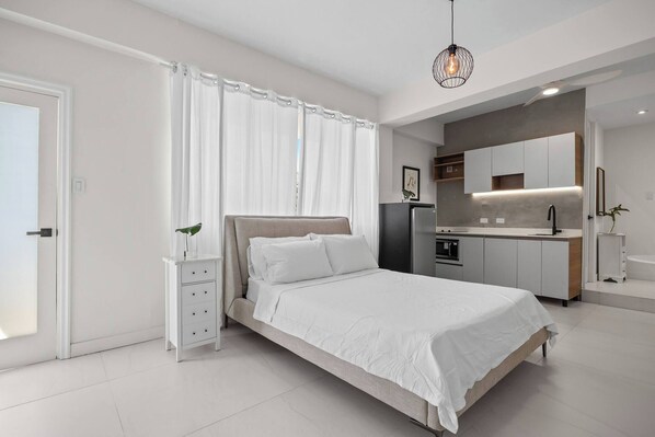 A modern bedroom with a bed, bedside table, and a built-in kitchen area. - Naya Sanctuary - Serena 1 (San Juan city)