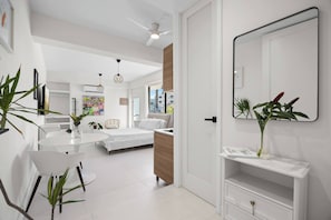 A modern, well-lit room with a bed, a dining table with chairs, a white TV, and a large mirror. - Naya Sanctuary - Serena 1 (San Juan city)
