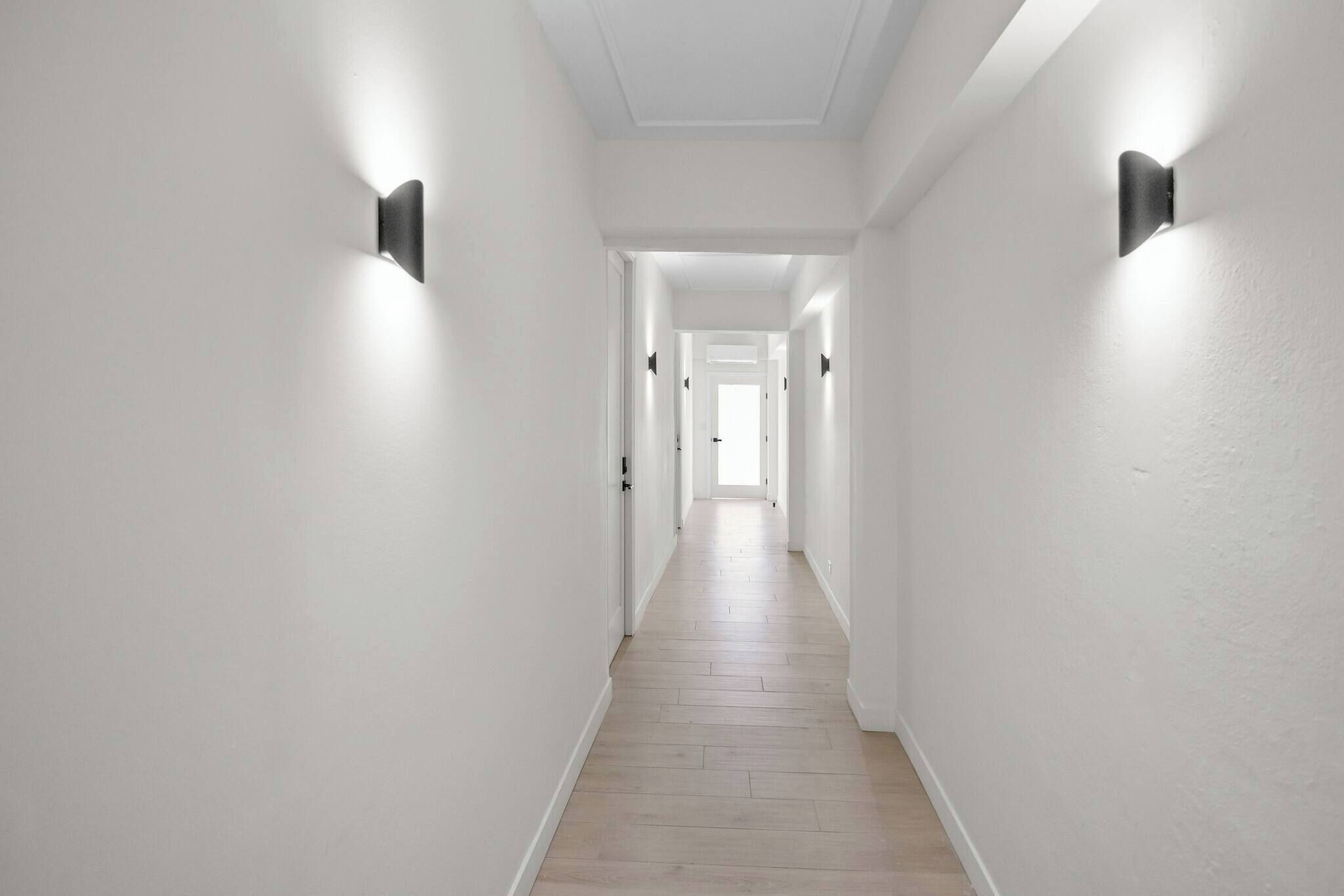 Un pasillo con paredes blancas y suelo de madera, que conduce a una puerta al final.