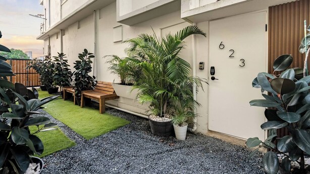 Un edificio residencial con fachada blanca, una puerta con números, un banco y plantas en macetas.
