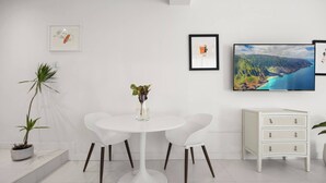 Una habitación moderna con una mesa redonda blanca, dos sillas blancas, un mueble blanco pequeño y obras de arte enmarcadas en la pared.