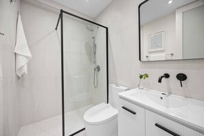 A modern bathroom with a glass-enclosed shower, a white toilet, a white sink, and a mirror. - Naya Sanctuary - Serena 1 (San Juan city)