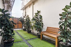 Un petit espace patio avec un banc en bois, des plantes en pot et une petite portion de gazon artificiel.