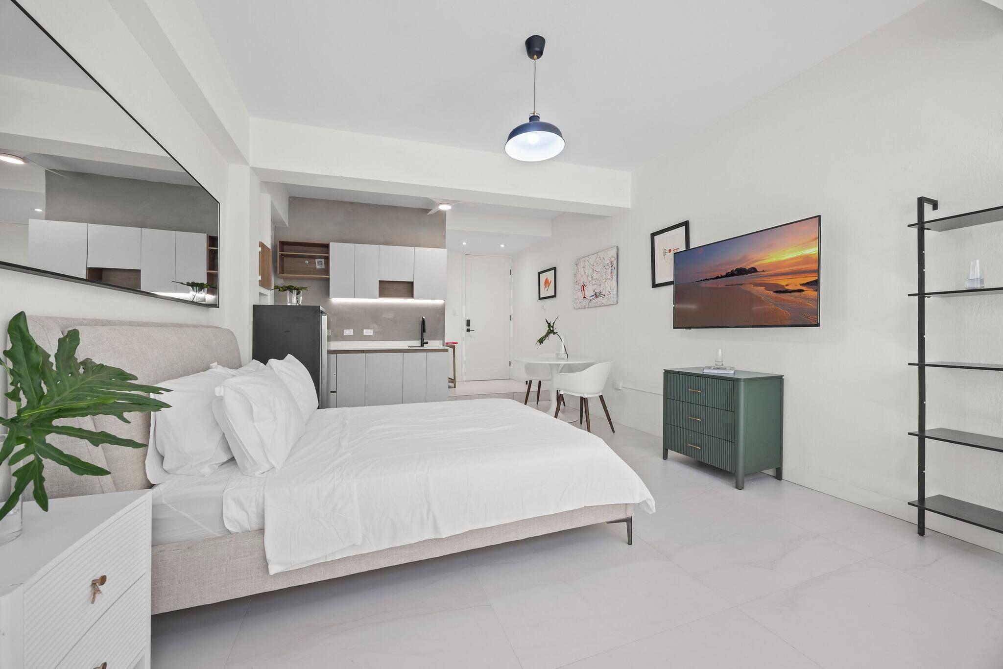 Une chambre moderne comprenant un lit, un bureau, une chaise, une armoire, un téléviseur et une plante.