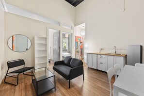 A modern living room with a sofa, a glass coffee table, a black chair, a white dining table, and a kitchen area with a sink and cabinets. - Barrio Sanctuary - Luna (San Juan city)