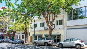 A street view with parked cars, a tree, and a building with a white facade and green windows. - Barrio Sanctuary - Luna (San Juan city)