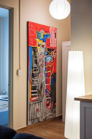 Une pièce avec une peinture abstraite aux couleurs vives accrochée au mur, une lampe blanche et un plancher en bois.
