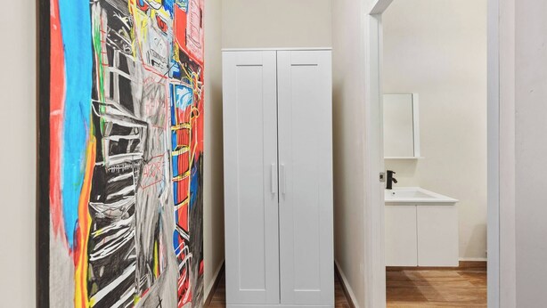 A hallway with a white wardrobe, a colorful abstract painting on the left, and a white sink with cabinets in the background. - Barrio Sanctuary - Luna (San Juan city)